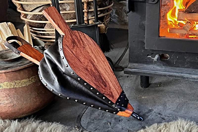 Handmade teak bellows leaning against a fireplace.