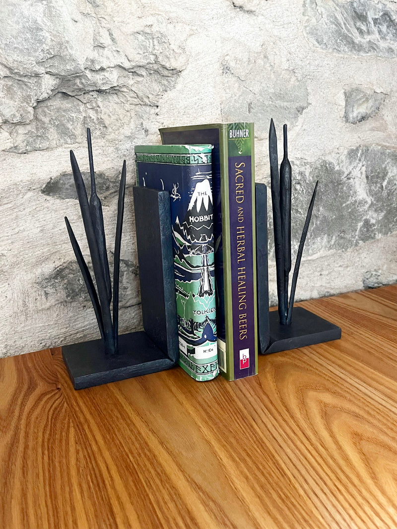 Forged iron bullrush bookends holding books on a wooden surface with a stone wall background