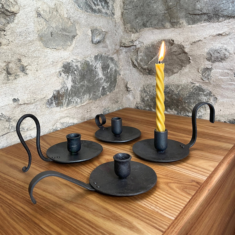 Set of forged metal candle holders on a wooden surface with a stone wall background