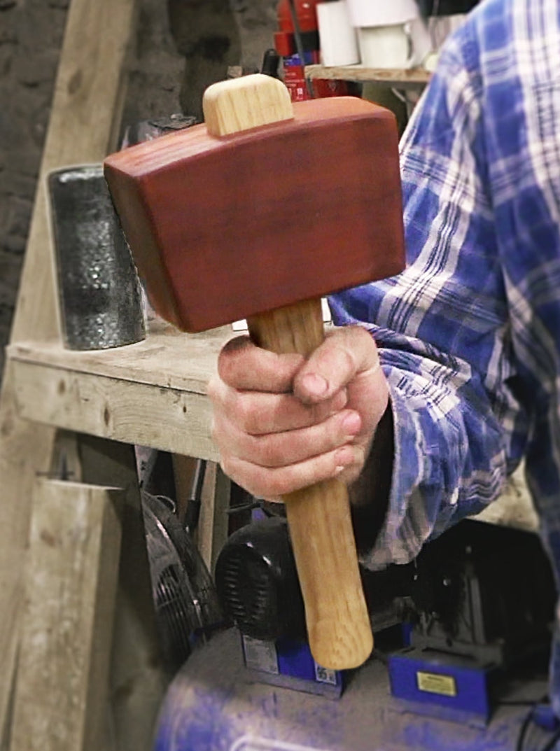Hand holding a wooden mallet over a blue Draper tool
