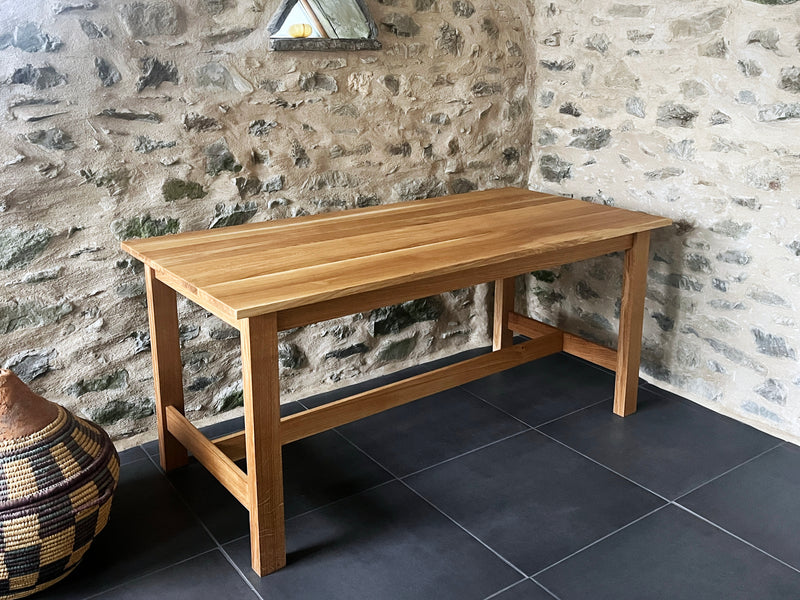 Oak table against a stone wall with a decorative basket on the floor.