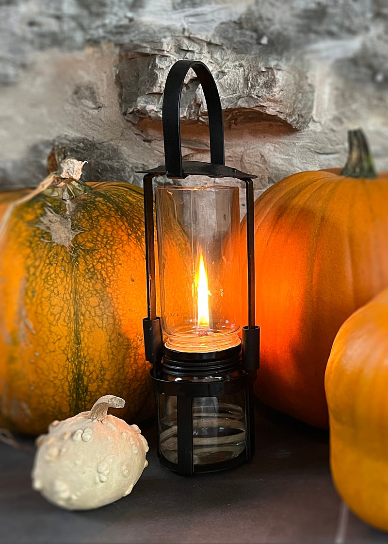 Black lantern with a lit candle surrounded by pumpkins against a stone wall background