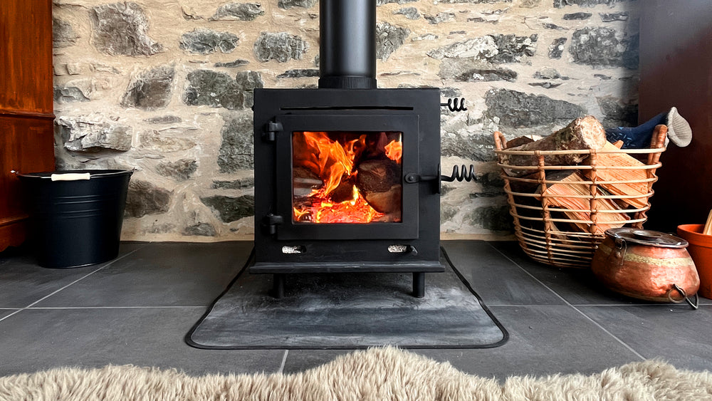 Wood-burning stove with flames inside, surrounded by a stone wall and wooden furniture.